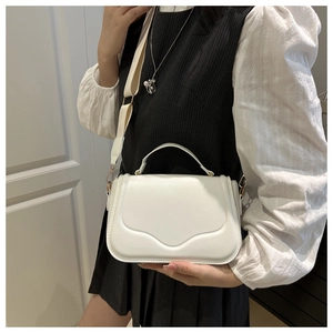 Detail view of a white minimalist bag with wave-edge flap and wide fabric shoulder strap