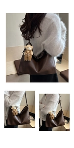Detail of a large brown tote bag featuring a cute bear charm with fashion inscription