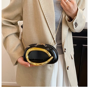 Detail of a black patent leather mini crossbody bag with a large gold metal buckle