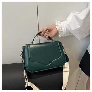 Detail of dark green leather handbag with cream wide shoulder strap and gold hardware