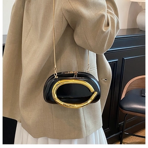 Detail of a shiny black patent leather crossbody bag with a large gold metal handle accessory