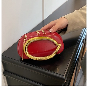 Detail of red glossy leather handbag featuring a large golden circular handle and chain
