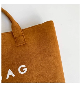Detail of camel suede tote bag showing reinforced stitching and white BAG text print
