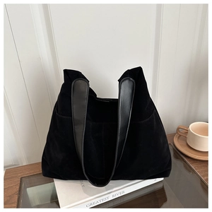 Detail of matte black tote bag showing side pockets and leather straps on wooden table