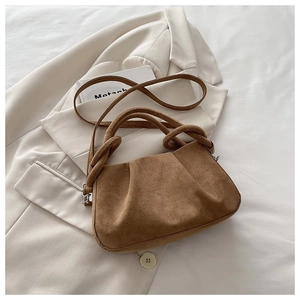 Detail of brown suede tote with pleated texture and decorative knotted handle on beige blazer