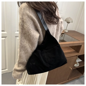 Side view of black matte leather tote bag worn by model in a cozy indoor setting