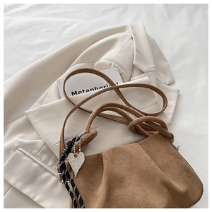 Detail of brown suede handbag featuring pleated design and heart-shaped silver charm