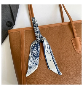 Détail d'un foulard en soie noué sur la poignée d'un sac en cuir avec motif bleu