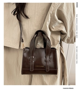 Detail of dark brown glossy patent leather bag with gold hardware and shoulder strap