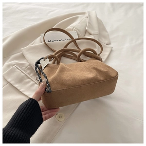 Detailed shot of brown pleated suede bag featuring silver heart pendant and knot detail