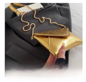 Detail of gold epi wave texture and metal sphere chain on stylish mini envelope bag