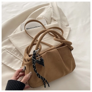 Detail of brown suede handbag featuring a twisted handle and black heart charm detail