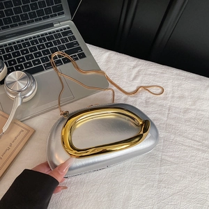 Silver metallic pebble clutch with gold handle and snake chain strap in a modern setting