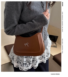 Detail of a brown saddle bag featuring a silver metal bow on a knit sweater background