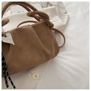 Detail of brown suede handbag with heart metal charm and striped woven strap