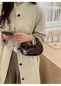 Dettaglio borsa a mezzaluna in pelle verniciata marrone scuro con logo testuale bianco