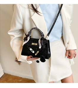 Detail of black crocodile texture handbag with gold clasp and silk scarf handle