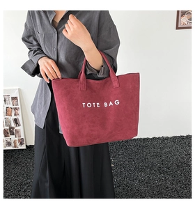 Détail du sac fourre-tout bordeaux en daim avec lettrage TOTE BAG porté à la main par un modèle