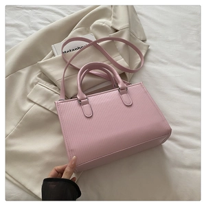 Dettaglio borsa quadrata rosa con texture verticale su un abito beige e un libro