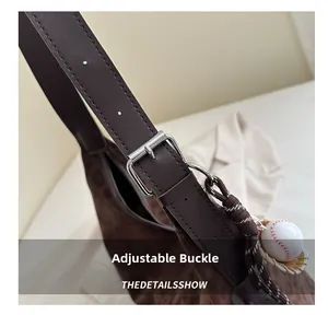 Detail of dark brown suede shoulder bag with adjustable buckle strap and baseball charm