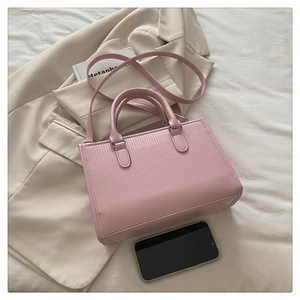 Vista piatta di una borsa tote quadrata rosa chiaro con strisce verticali sul letto