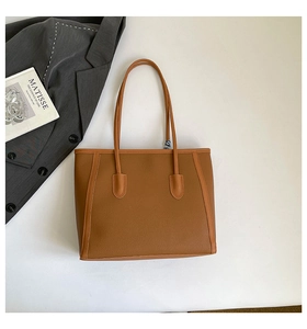 Détail du sac cabas marron à texture litchi à côté d'un blazer et d'un livre