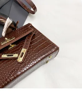 Detail of crocodile embossed brown handbag featuring golden twist lock and silk scarf decor