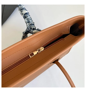 Détail du sac cabas en cuir marron avec fermeture éclair dorée et foulard en soie décoratif