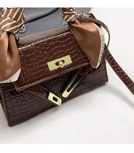 Detail of dark brown faux crocodile leather handbag with gold lock and silk scarf