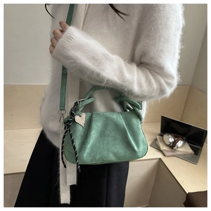 Detail of green pleated velvet handbag with polka dot ribbon and heart charm