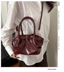 Macro shot of dark red glossy handbag featuring pleated texture and metal buckle