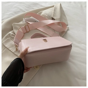 Pink crossbody bag with wide fabric strap and golden U-shaped buckle on beige blazer