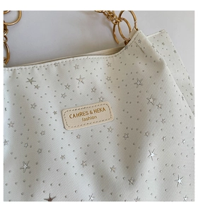 Detailed close-up of white textured tote with silver star studs and gold chain handle