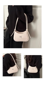 Detail of off-white shoulder bag featuring a metal bow accent and knotted strap detail