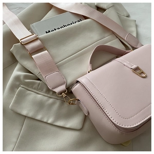Pink leather crossbody bag detail with wide woven strap and gold buckle on a beige suit