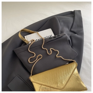 Detail of gold envelope chain bag featuring wave textured pleats on gray suit background