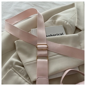 Detail of pink nylon shoulder strap with gold adjustable buckle on a beige blazer background