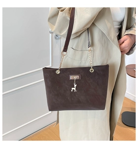 Detail of deep brown suede tote bag with golden deer pendant and metal chain strap