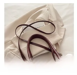 Detail view of burgundy leather bucket bag with slim shoulder strap on beige blazer