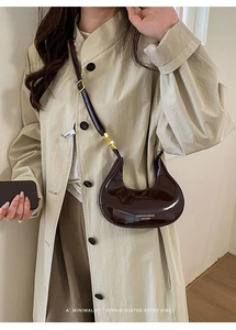 Dettaglio della borsa a mezzaluna in vernice marrone scuro su modella con trench beige