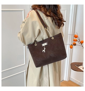 Detail of dark brown suede tote bag with golden deer pendant and chain shoulder strap