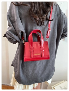 Detail of red faux leather handbag with golden Fashion & Bags logo and metal hardware