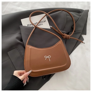 Detail of a brown leather shoulder bag with a metallic silver bow clasp on a grey suit