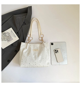 Detail of white tote bag with silver stars, gold rings and chic fashion accessories