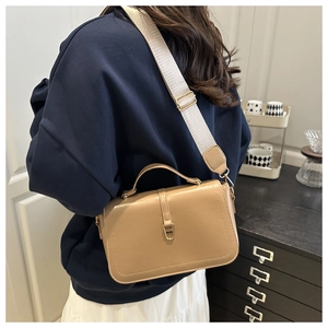 Detail of camel leather handbag featuring wide textile strap and gold metal buckle