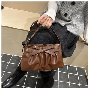 Detail of brown pleated tote bag with bow knot and silver star rivets held by model