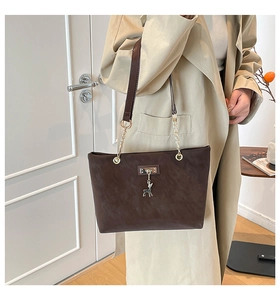 Detail of dark brown matte leather tote bag with metal deer pendant and chain strap
