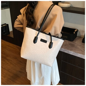 Detailed close-up of embossed texture and black contrast handle on a cream tote bag