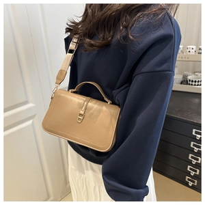 Detail of khaki crossbody bag with wide strap and metallic clasp in a home setting
