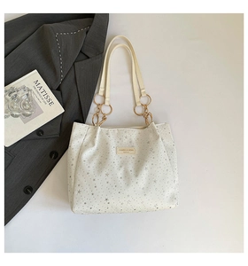 Detail of white star-print tote bag with chain strap and metallic ring design